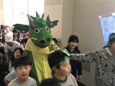 TKRの緑のドラゴンの着ぐるみと、校内で活動する子どもたち